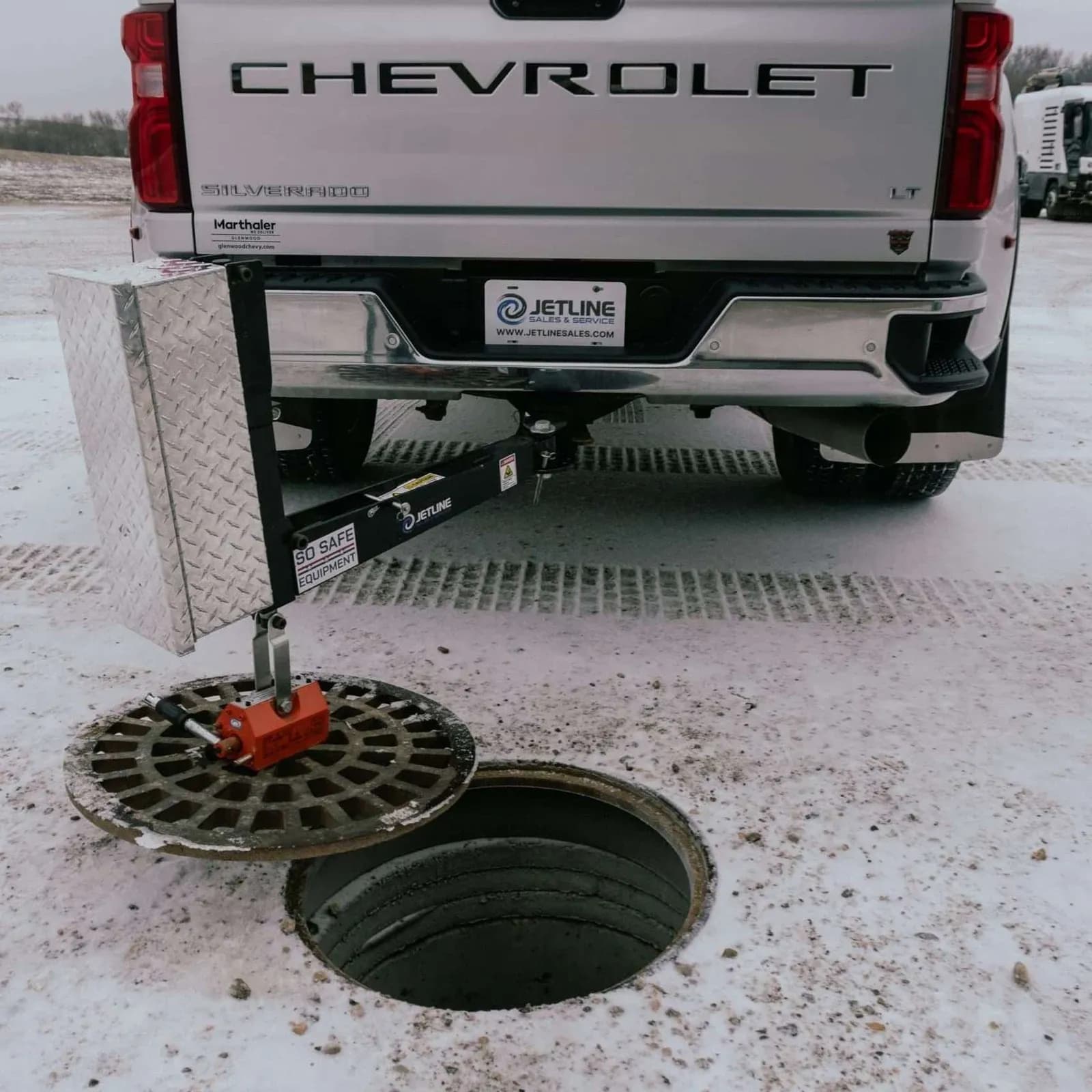 PowerLifter behind a pickup with a cover suspended beside an open manhole.