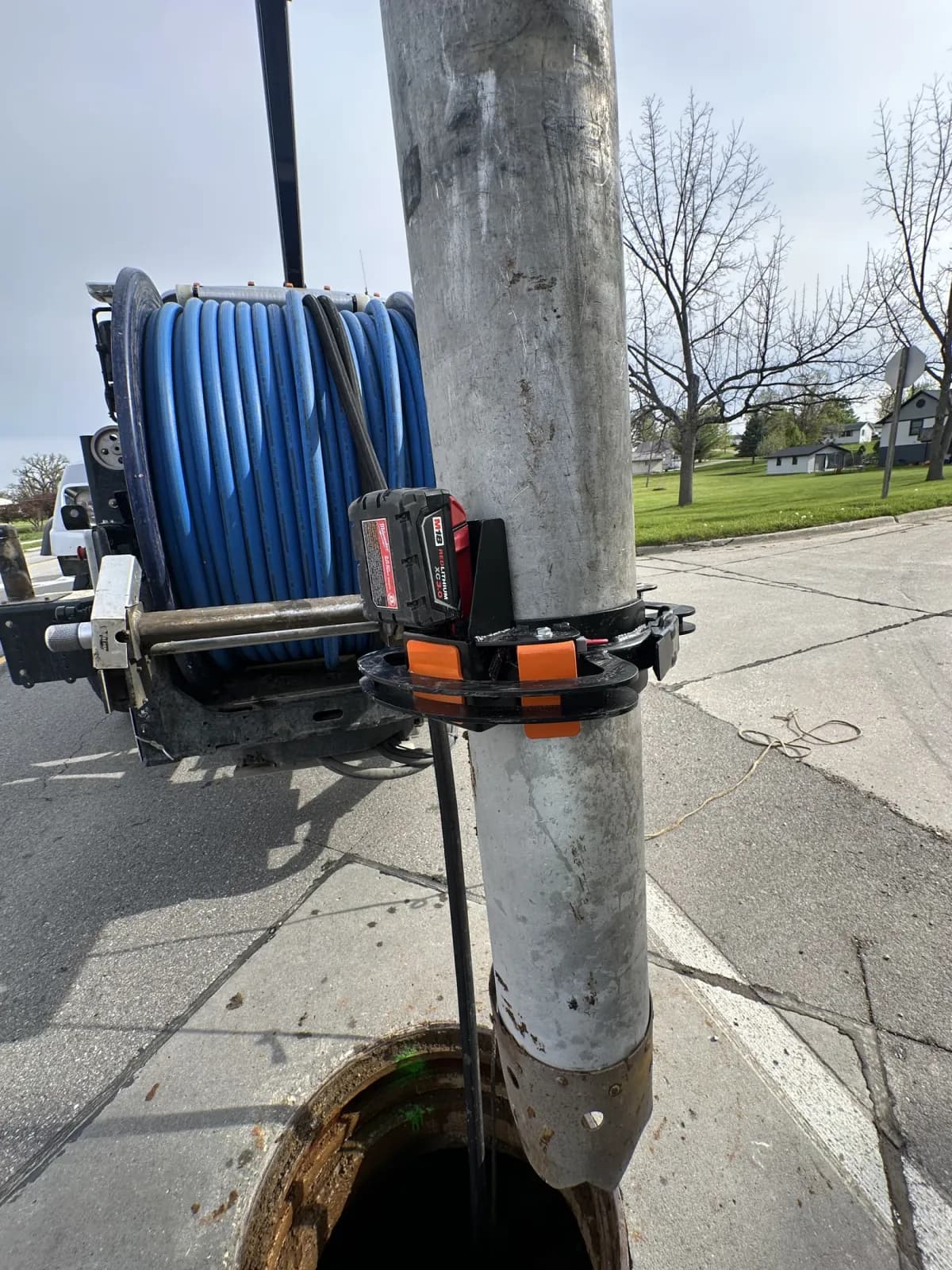 Black Torch clamp and battery on a vertical vacuum tube above a manhole.