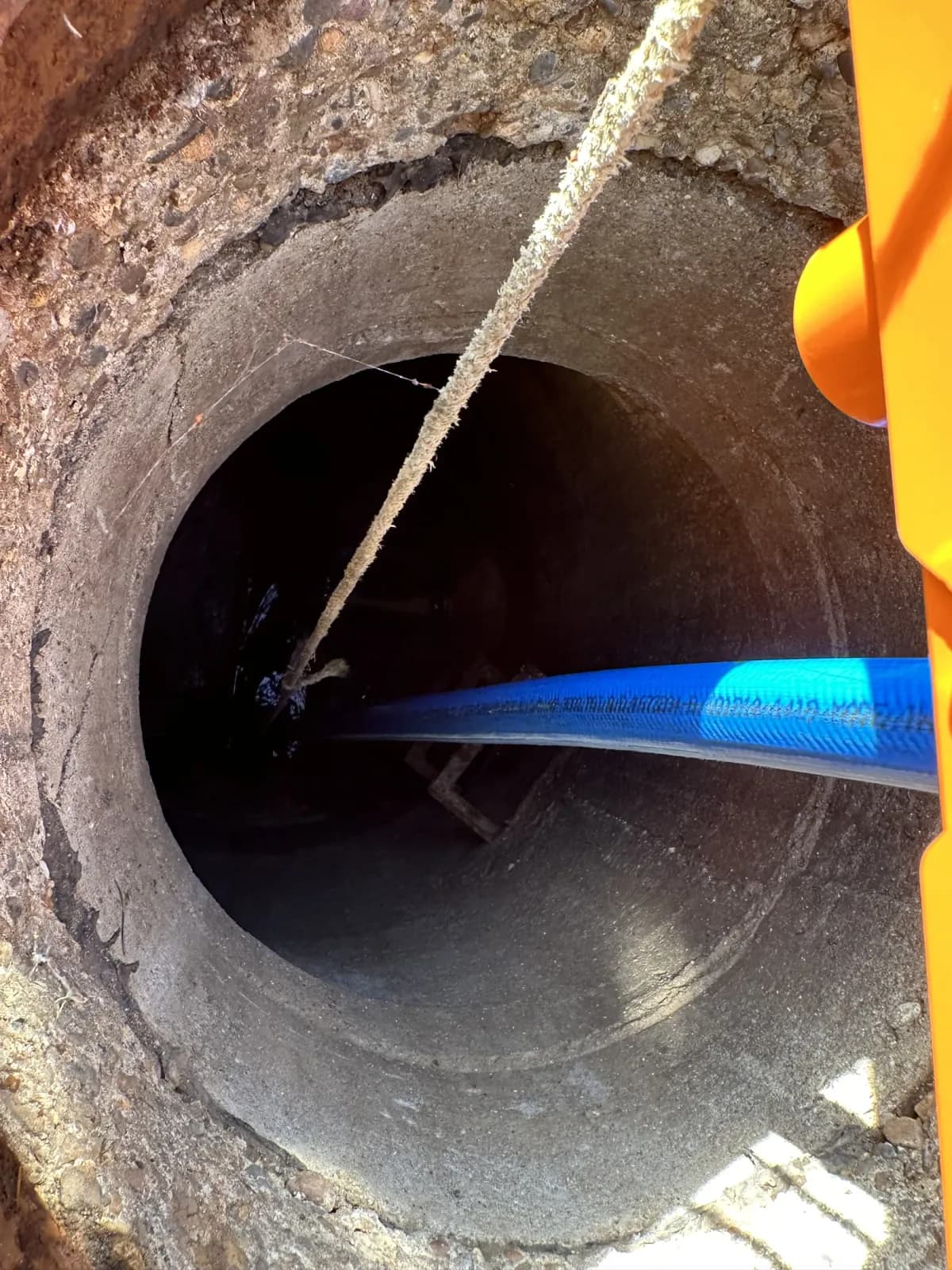 Blue hose and equipment line inside a manhole with the orange TorchRail at the edge.