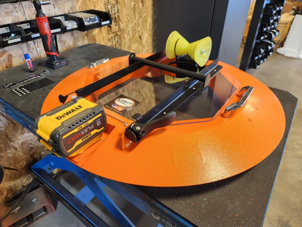 Manhole safety tool with bright orange frame, integrated roller guide, plexiglass shield, and DeWalt battery system for field use.