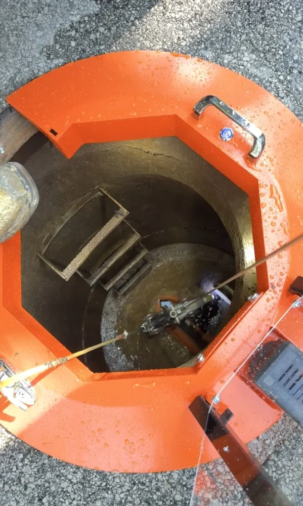 Field view of the Light Ring in use over a manhole during active water jetting, showing shield, hose rollers, and safety cover