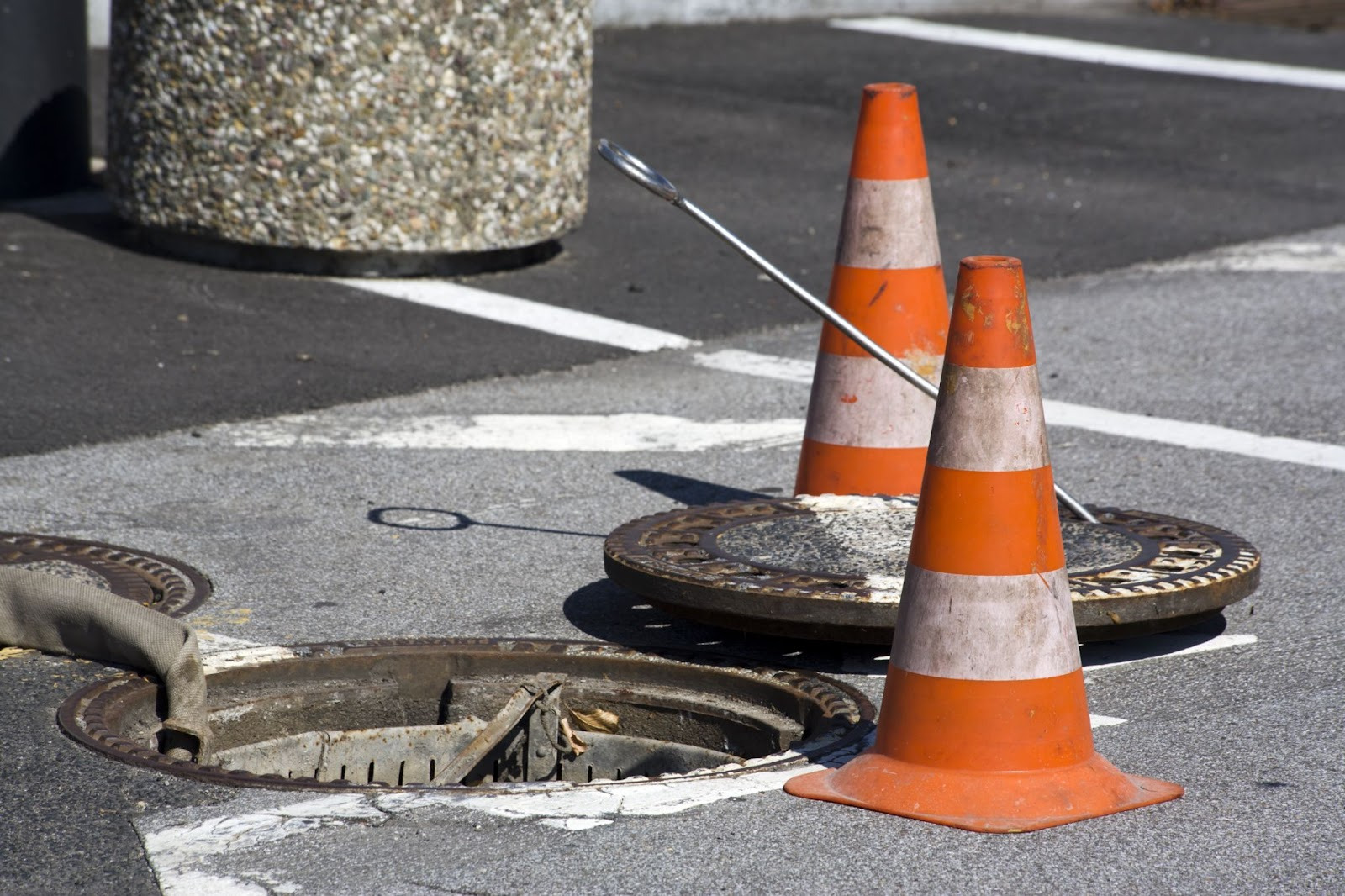Open manhole in active roadway with traffic cones illustrating utility worker manhole safety conditions