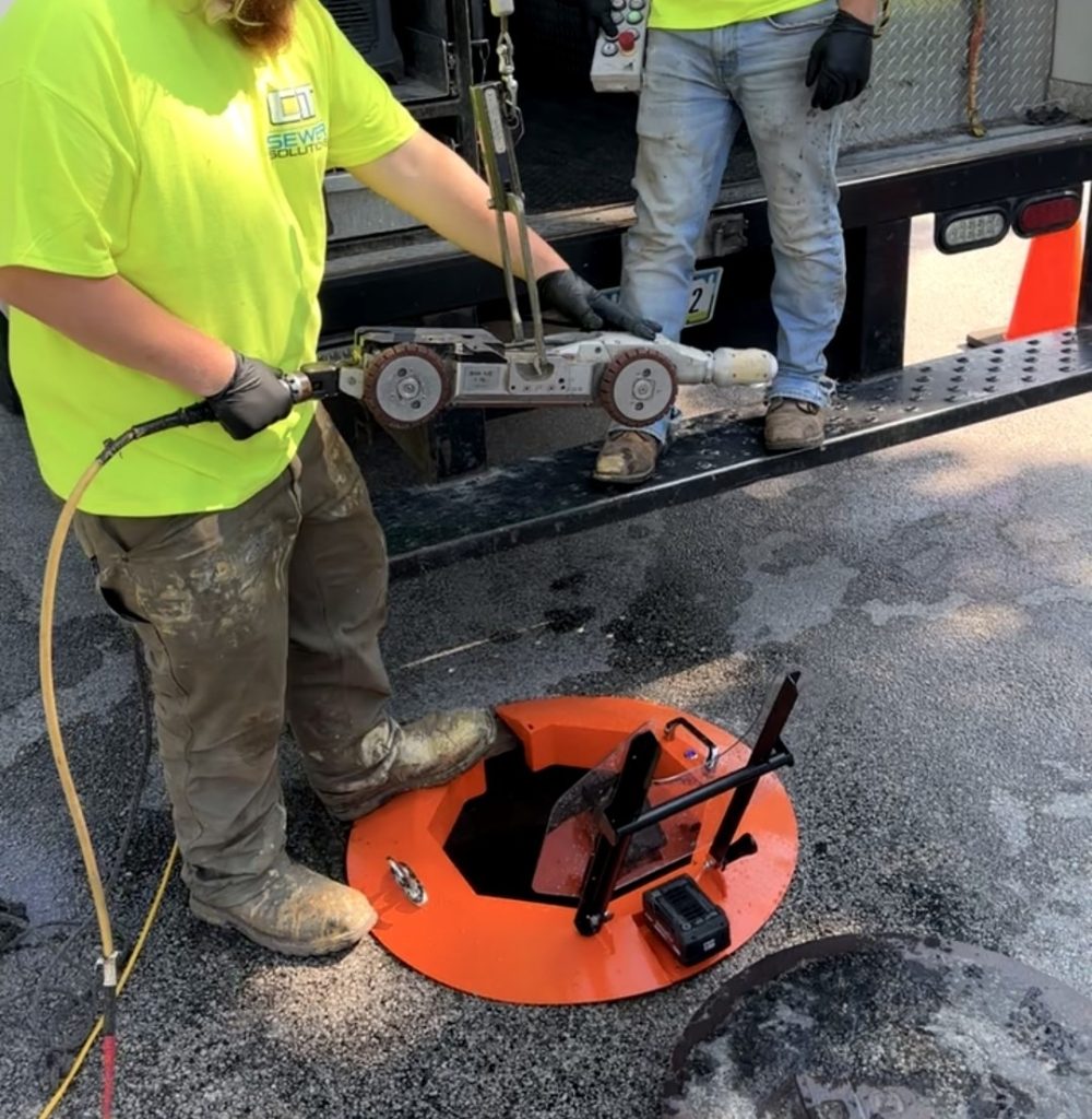 Light Ring Inc. crew deploying the Light Ring manhole protection system over an open manhole during active field operations, with jet truck and equipment in background.