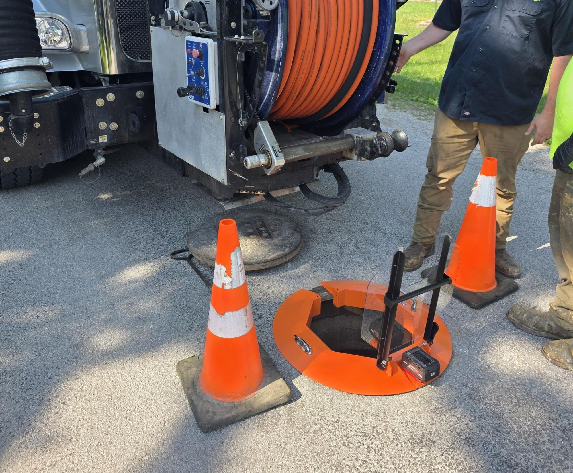 Light Ring manhole cover ring deployed over open manhole at jet truck jobsite with traffic cones and jetting hose reel visible.