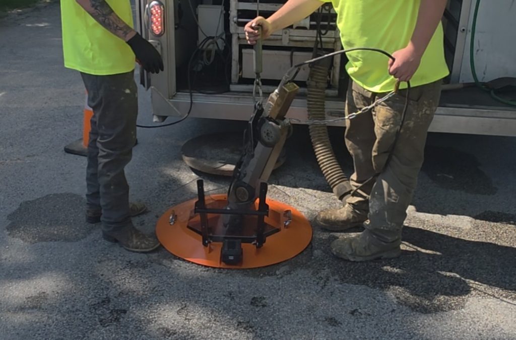 Two utility operators deploying a Light Ring integrated manhole protection system over an open manhole during routine maintenance work.