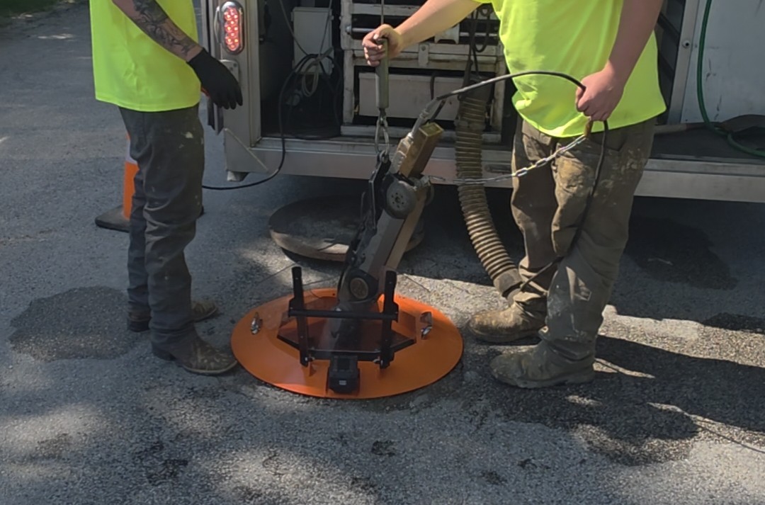 Two utility operators deploying a Light Ring integrated manhole protection system over an open manhole during routine maintenance work.